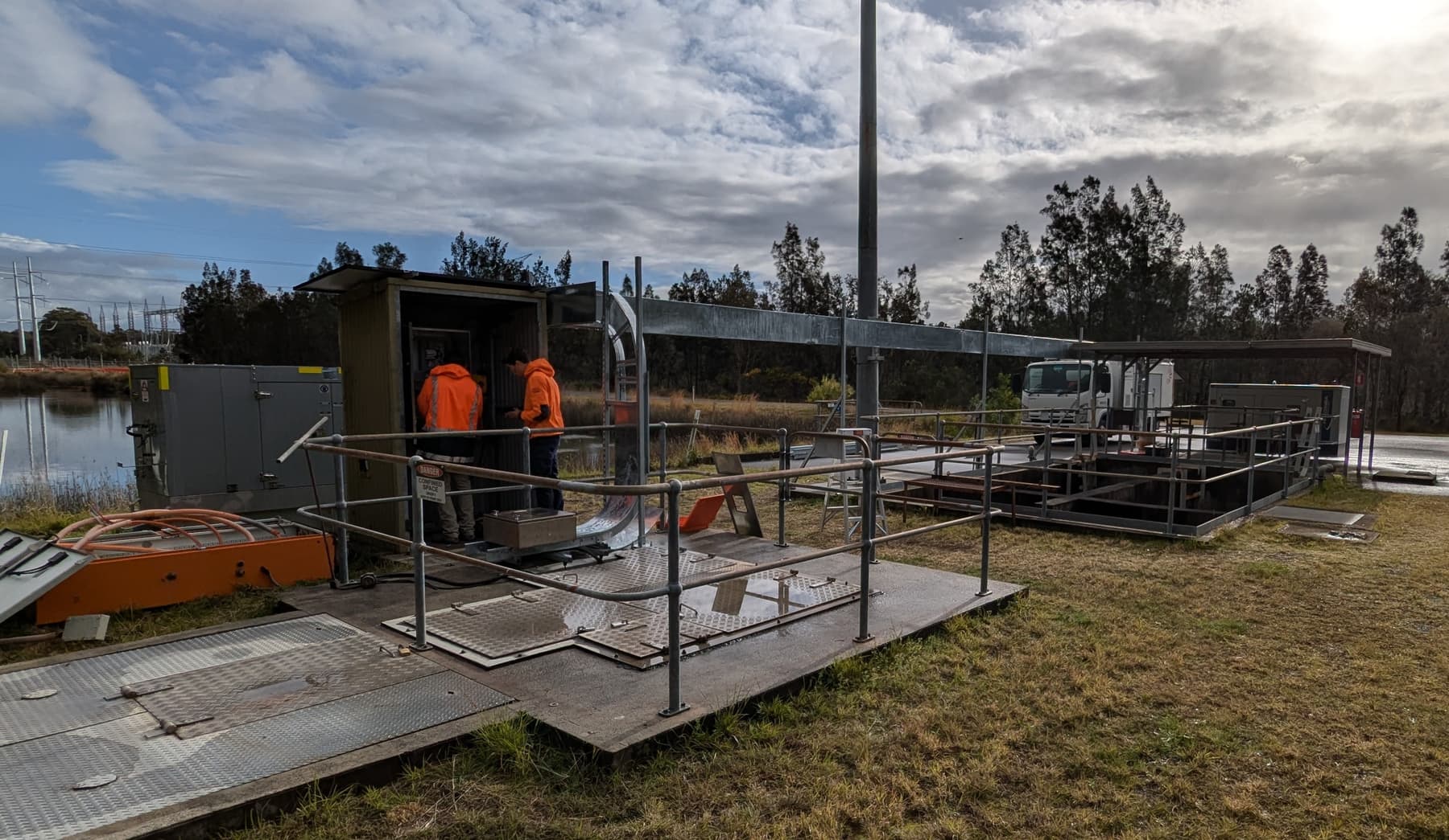 Two engineers working at the control cabinet on a pump station platform beside a dam