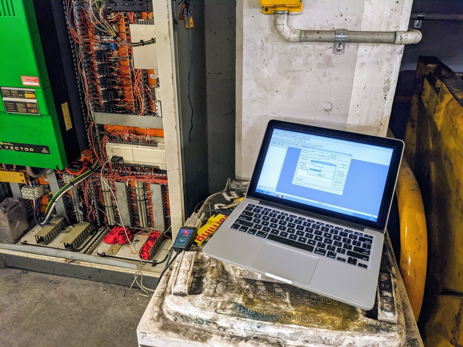 Old control cabinet with exposed wiring and a laptop connected